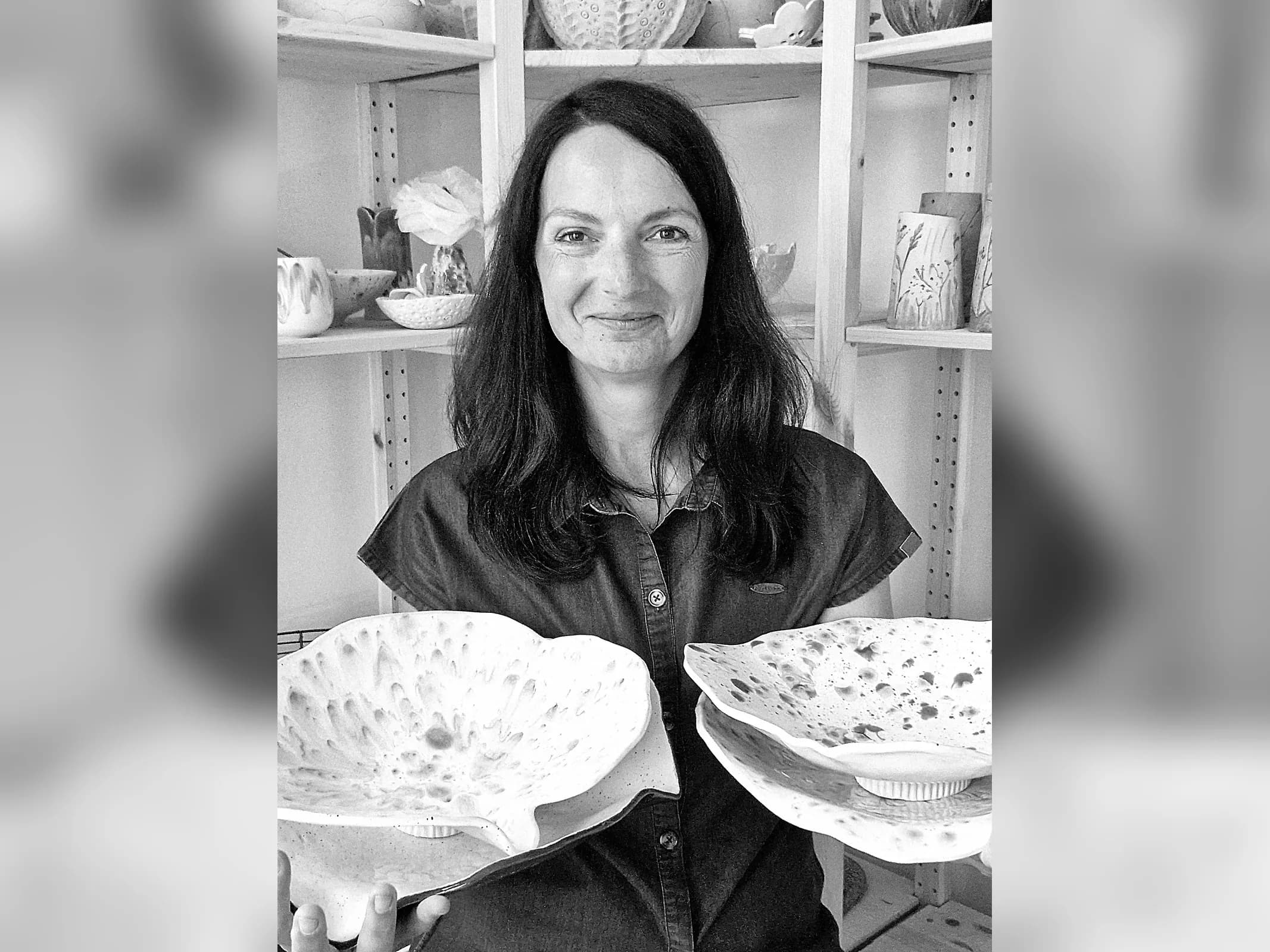 Heike Rippich hält zwei fertige Belly Bowls in den Händen und lächelt in die Kamera, dahinter die Regale ihrer Werkstatt